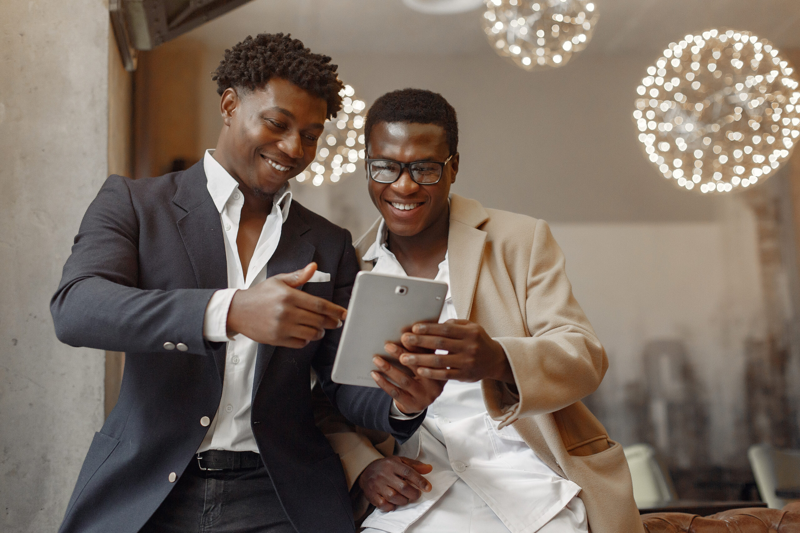 Black men in a cafe. Guy talking. Man in a black suit. Friends use the tablet.